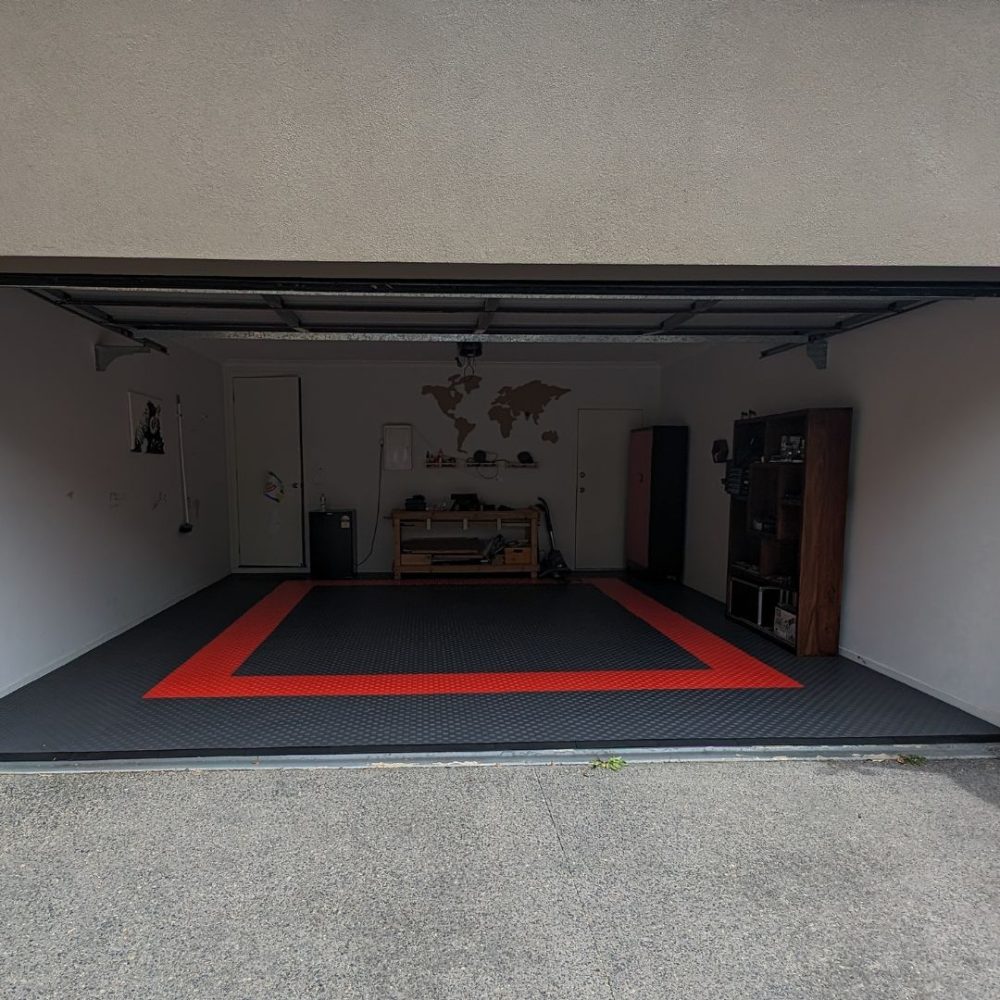 Flexspec DiamondFlex Pro solid garage floor tiles in black with a safety red border, installed in a home workshop with a workbench.